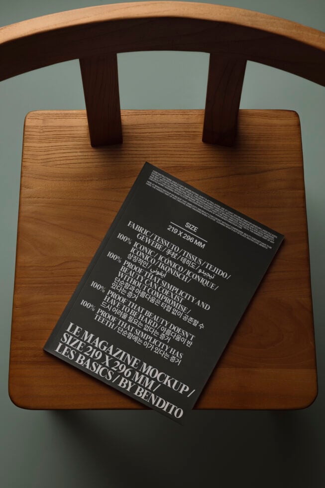 Black magazine mockup laying on wood chair seat with natural wood frame visible