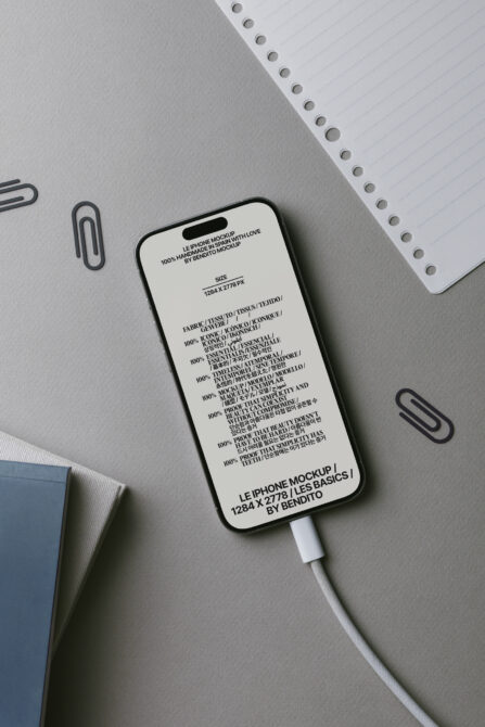iPhone mockup with white screen showing product specs, USB cable attached, surrounded by office supplies