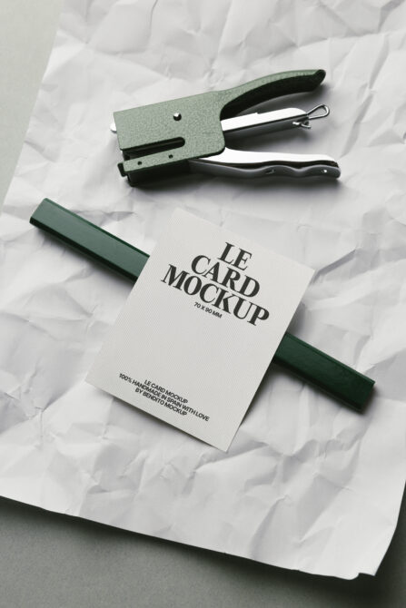 White card mockup with green fabric swatch, stapler, black handle on crumpled paper