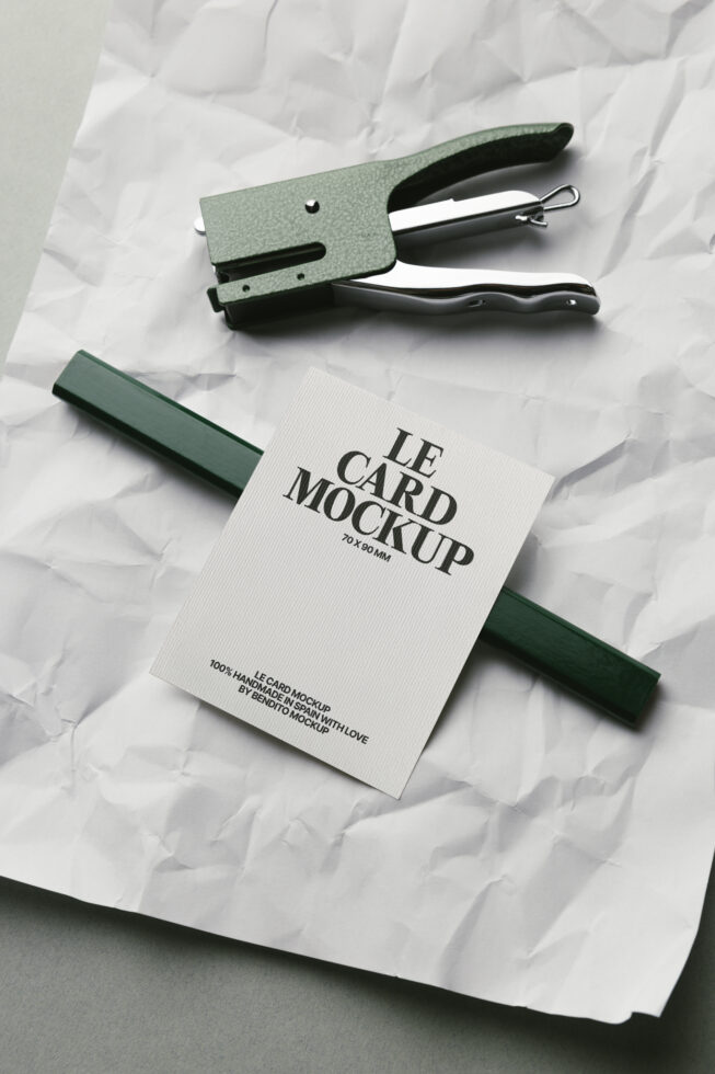 White card mockup with green fabric swatch, stapler, black handle on crumpled paper