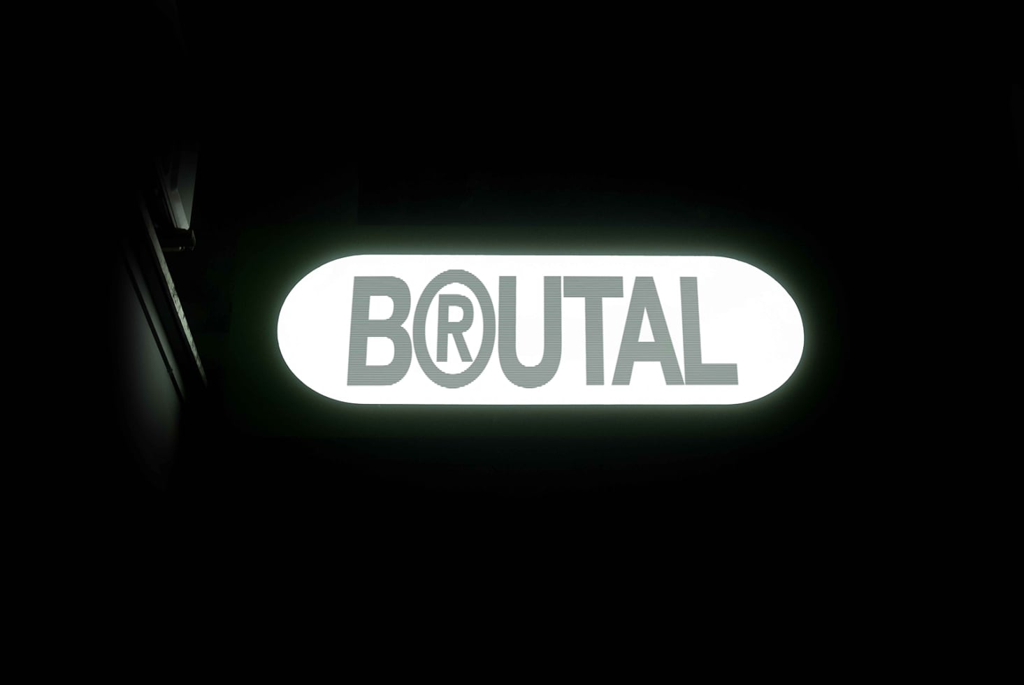 Glowing green neon sign reading BRUTAL on white rounded background