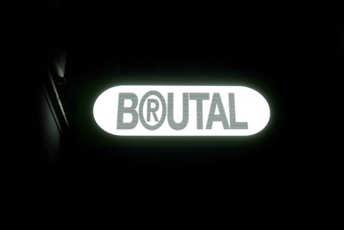 Glowing green neon sign reading BRUTAL on white rounded background
