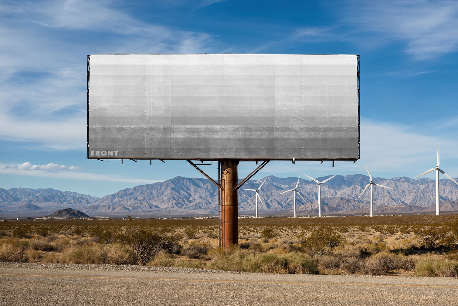Blank weathered billboard overlooking valley with wind turbines, mountains in distance