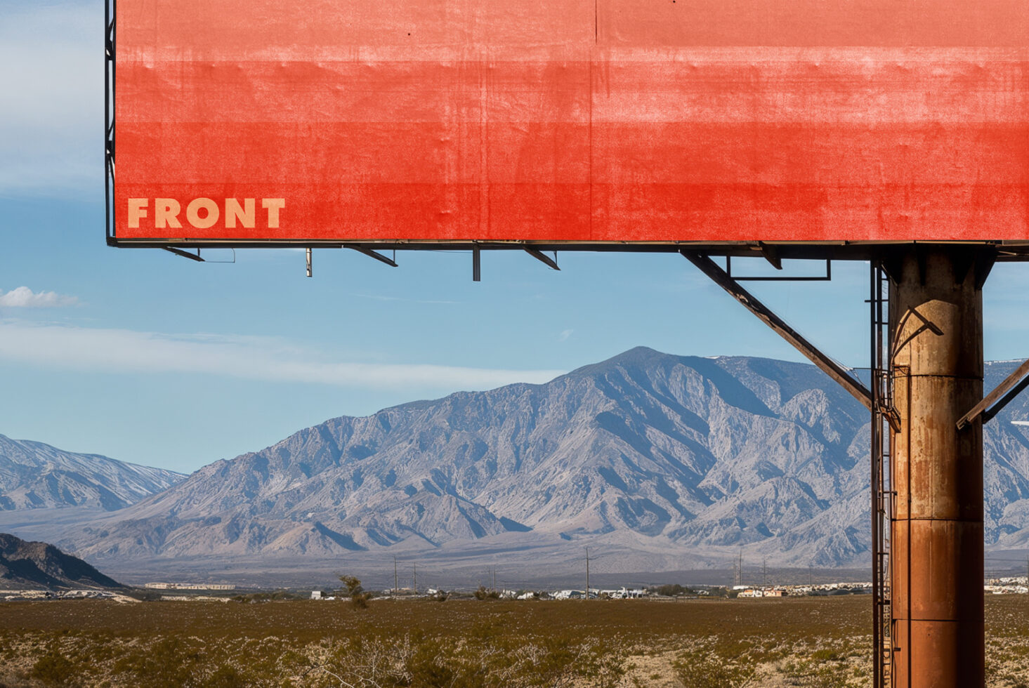 Bright red desert billboard with mountains, rusty support pole, sage brush landscape