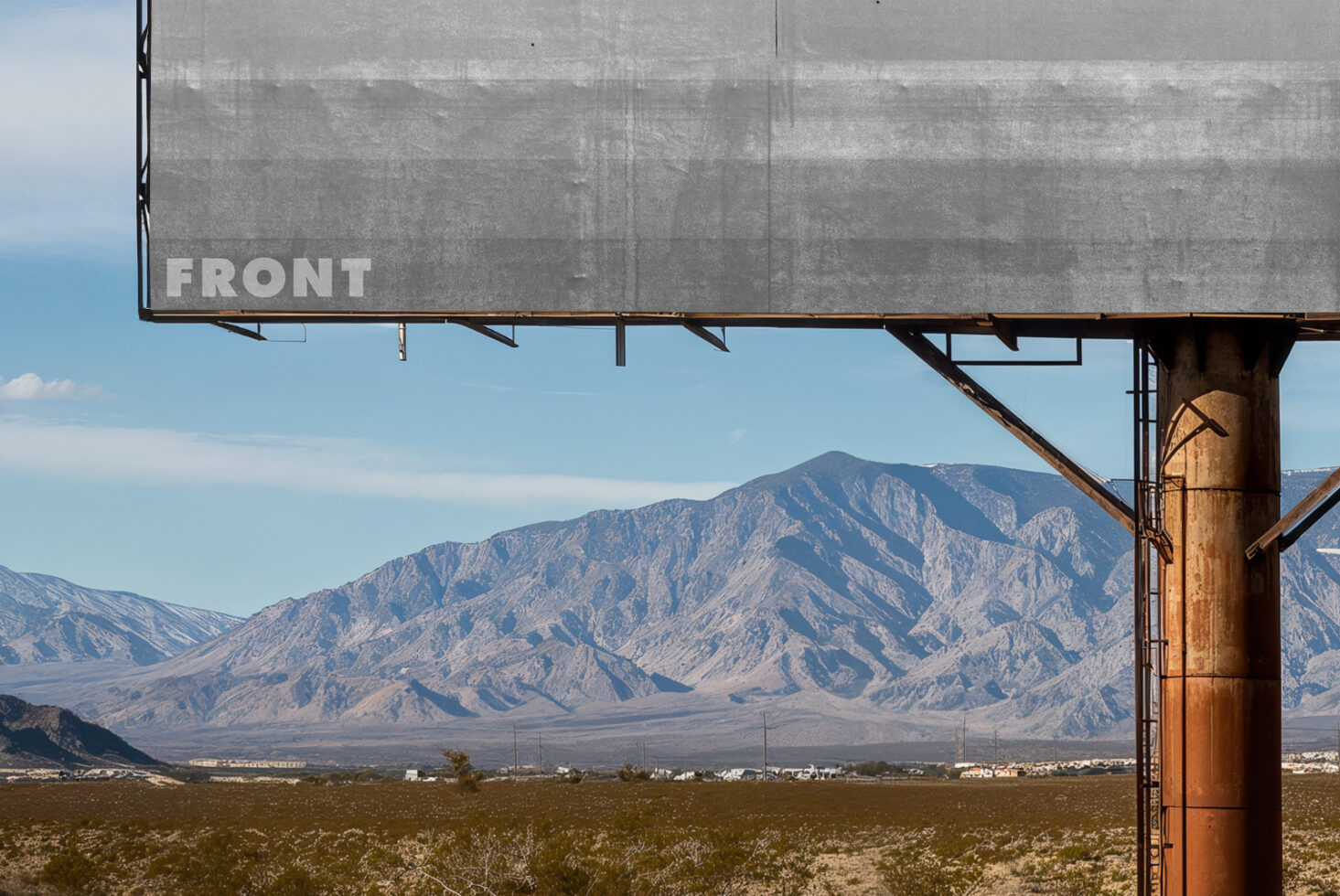 Weathered billboard mockup over rocky desert mountain range with blue sky overhead