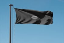 Black flag with cursive JAM logo waving against blue sky on metal pole