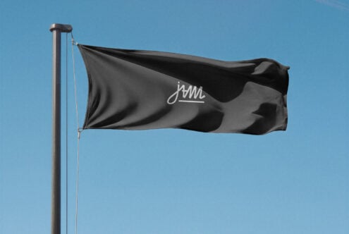 Black flag with cursive JAM logo waving against blue sky on metal pole