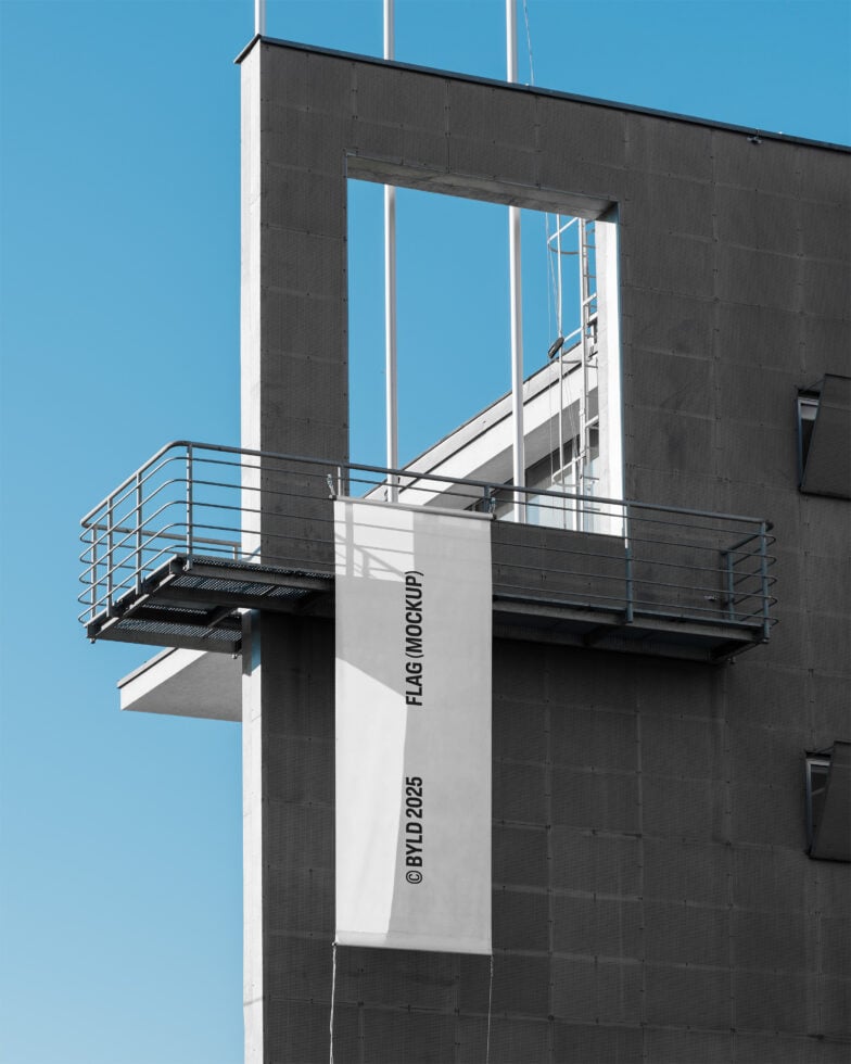 White vertical flag mockup hanging on industrial building against blue sky