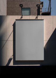 Blank billboard mockup on modern building facade with dramatic shadow, two spotlights above