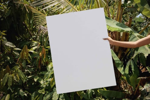 Blank white paper mockup displayed among green banana leaves in sunlight