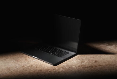 Black laptop on concrete ground with dramatic side lighting against dark background