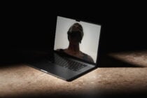 Black laptop displaying silhouette of woman's head on screen, concrete setting