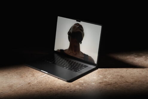 Black laptop displaying silhouette of woman's head on screen, concrete setting