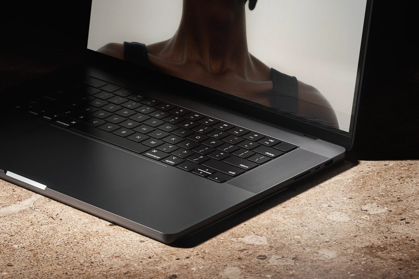 Laptop on concrete ground with person's silhouette reflecting on screen