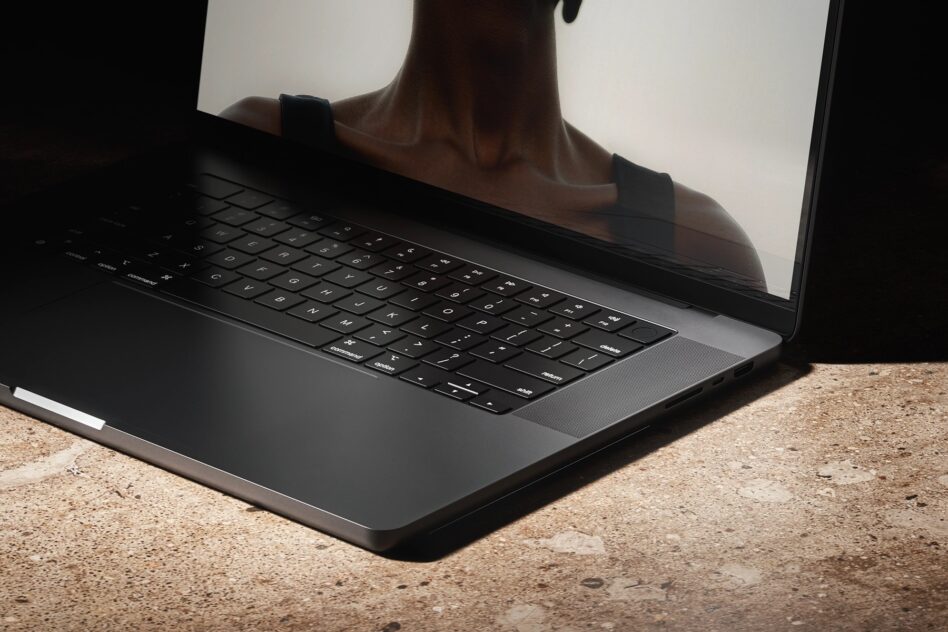 Laptop on concrete ground with person's silhouette reflecting on screen