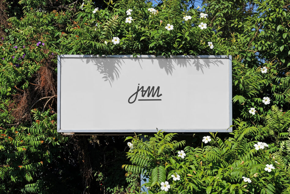 Light gray billboard mockup with handwritten script text among flowering shrubs