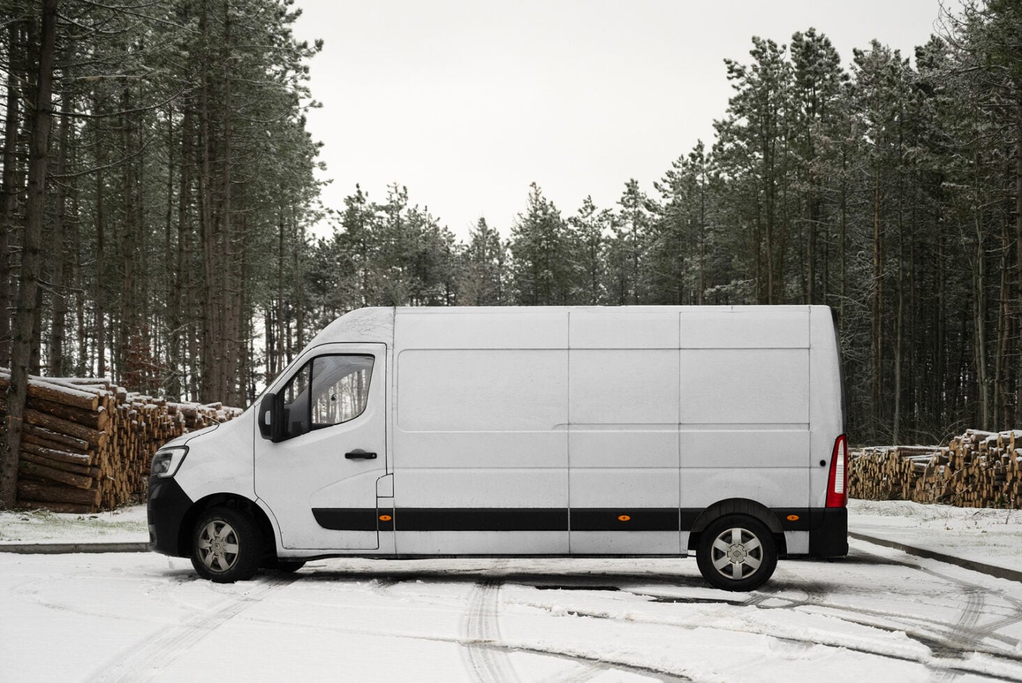 White cargo van parked in snowy industrial yard with lumber stacks nearby