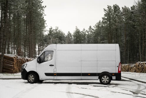 White cargo van parked in snowy industrial yard with lumber stacks nearby