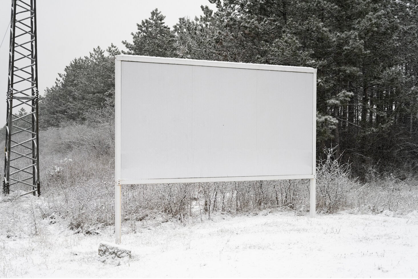 Blank roadside billboard in snowy winter forest setting ready for design