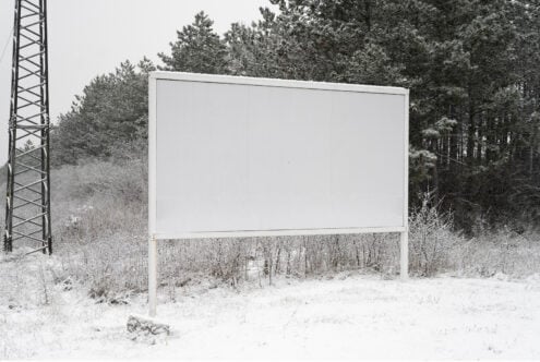 Blank roadside billboard in snowy winter forest setting ready for design