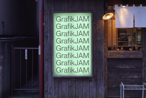 Neon green lightbox on dark wooden storefront displaying stacked GrafikJAM type