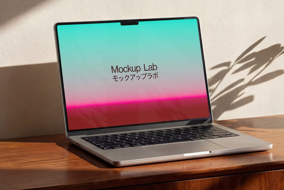 Laptop displaying cyan to pink gradient, angled view with afternoon light