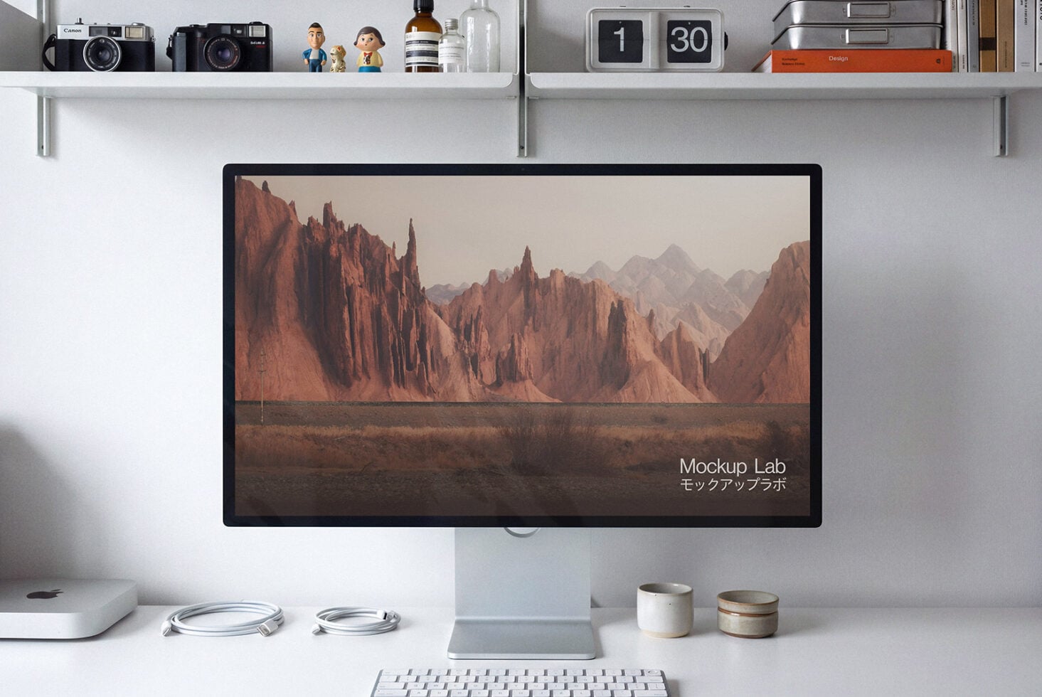 Desktop setup with monitor displaying desert landscape, shelves with cameras, books, plant