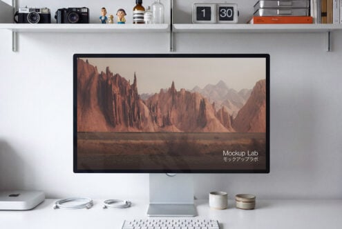 Desktop setup with monitor displaying desert landscape, shelves with cameras, books, plant