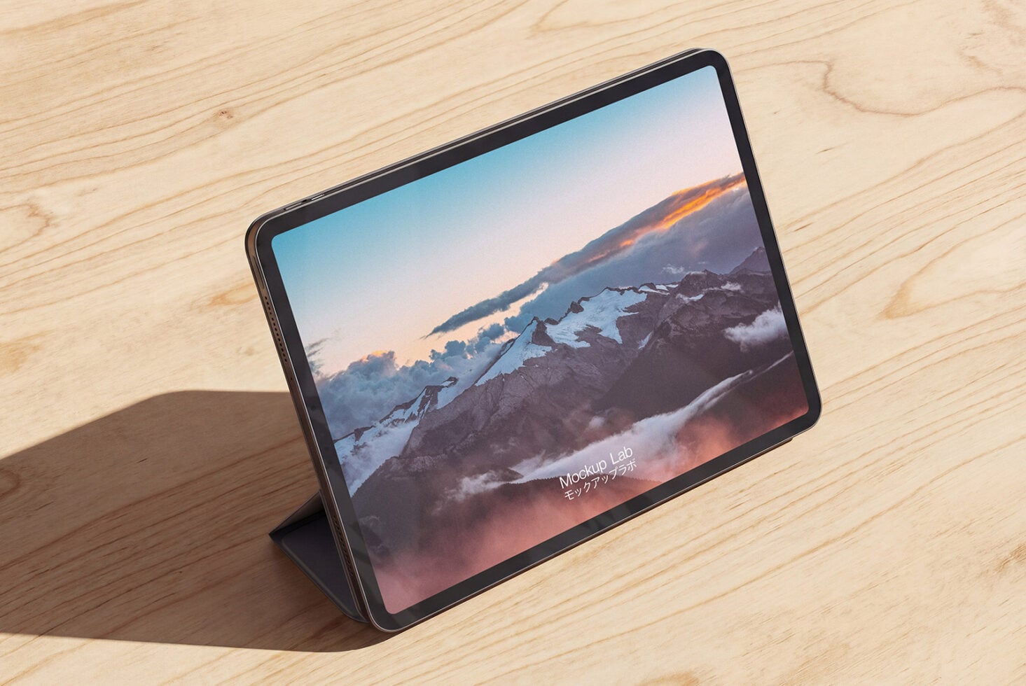 Tablet on wood surface displaying snowy mountain landscape at sunset with warm clouds