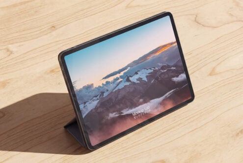 Tablet on wood surface displaying snowy mountain landscape at sunset with warm clouds