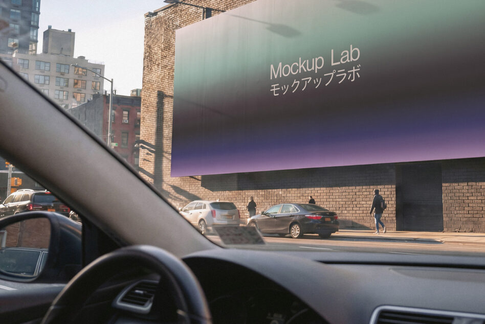 Car interior dashboard view of brick building with large digital billboard displaying Mockup Lab branding
