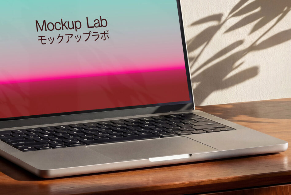 Laptop on wood desk showing gradient screen with plant shadow, side view