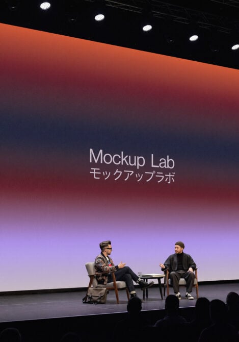 Two people on stage in conversation with red to blue gradient screen displaying Mockup Lab