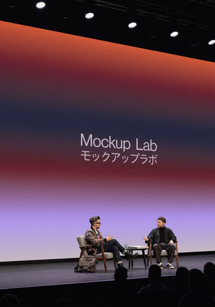 Two people on stage in conversation with red to blue gradient screen displaying Mockup Lab