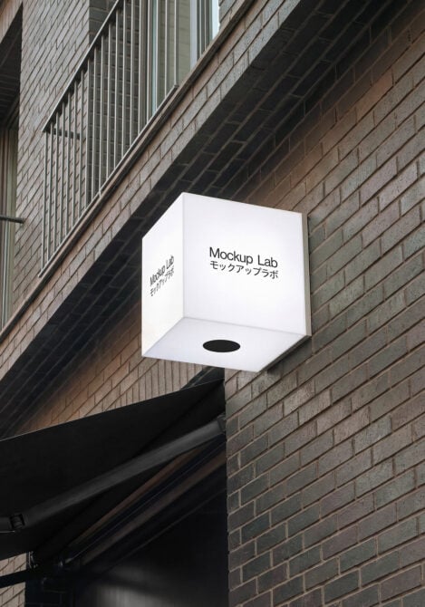 Glowing white cube hanging sign on brick facade showing Mockup Lab bilingual text