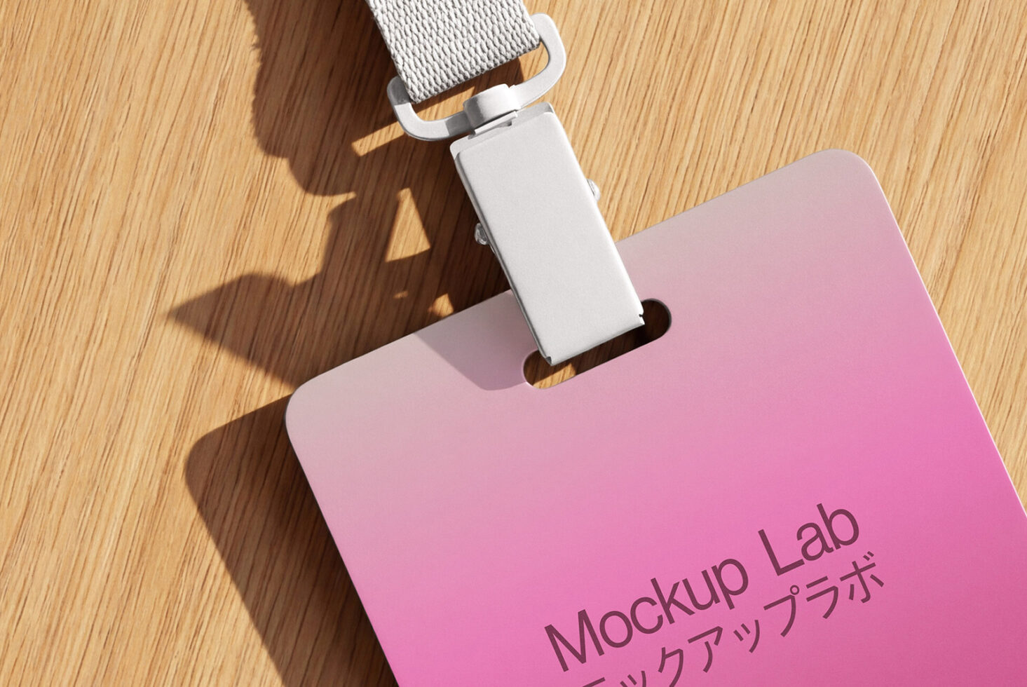 Pink ID badge with white lanyard on wooden surface catching sunlight