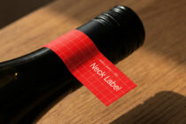 Wine bottle with bright red neck label showing white text on wooden surface
