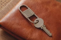 Metal padlock keychain on tan leather bag with circular engraved design