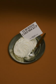Business card mockup leaning on metal plate with whipped cream on warm brown backdrop