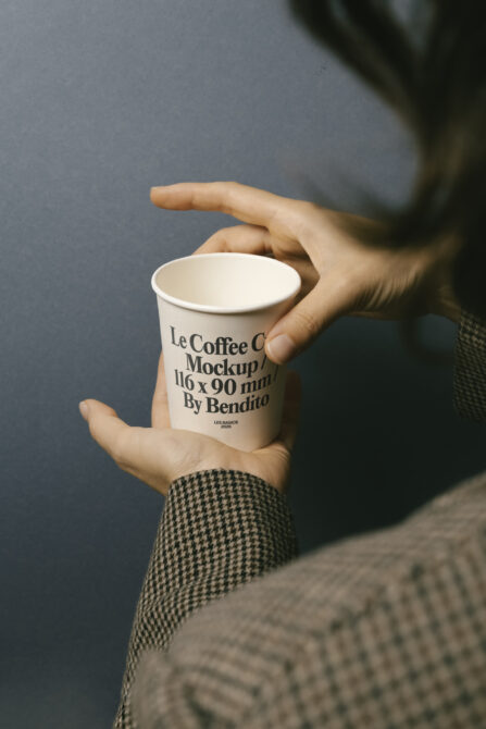 Person gripping paper coffee cup with printed logo in side view closeup