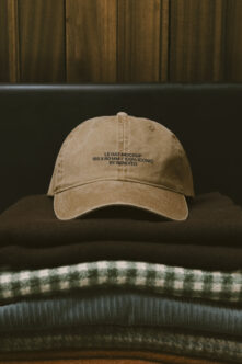 Tan washed cotton cap layered on sweaters in moody styled product scene