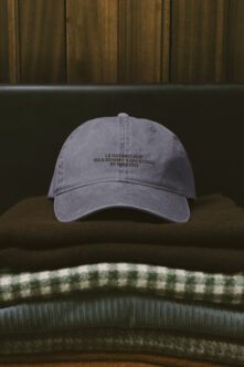 Slate blue washed baseball cap stacked on folded knitwear with minimal text