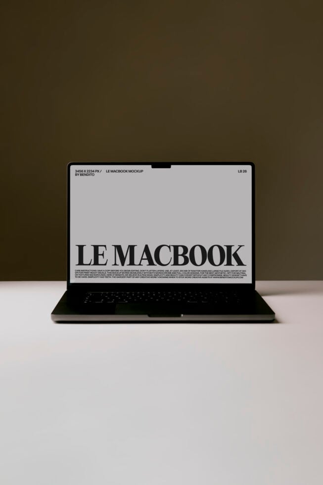 MacBook laptop open on white surface showing LE MACBOOK text on screen