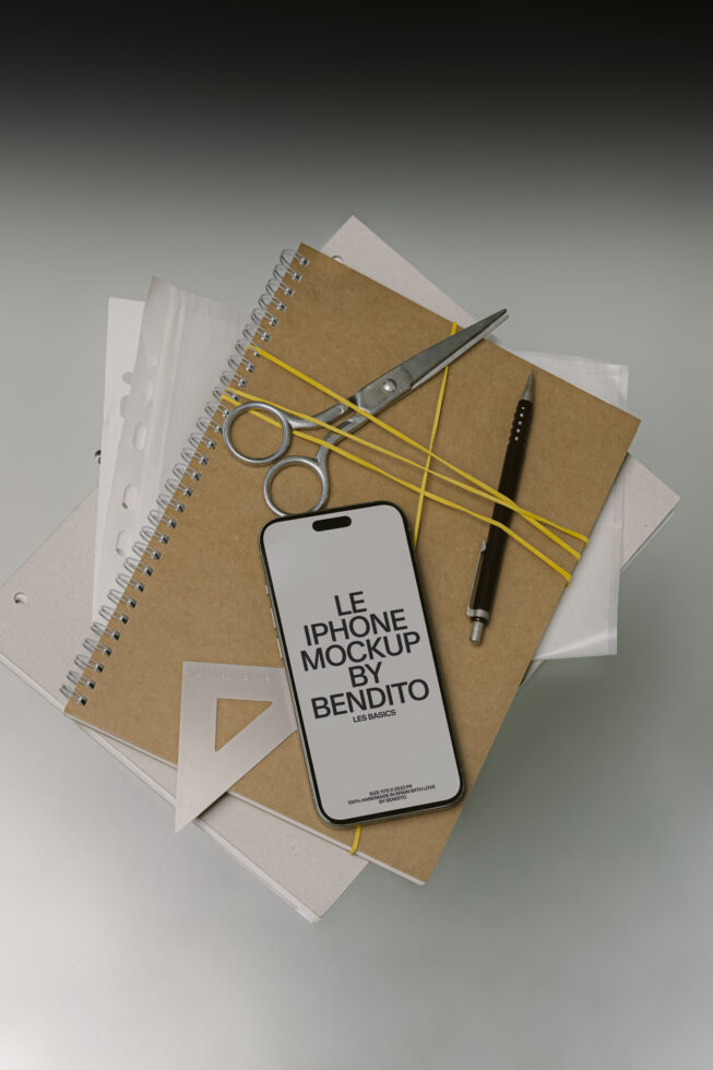 White phone mockup surrounded by kraft notebook, small scissors, yellow bands, pen