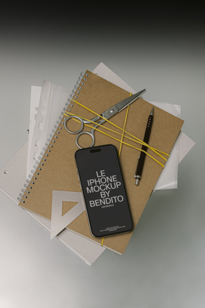 iPhone mockup flat lay with spiral notebook, scissors, yellow rubber bands, pens