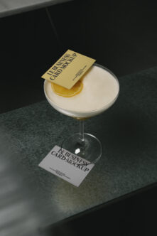 Gold business card mockup on cocktail glass with lemon slice, dark surface