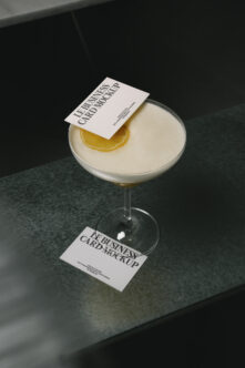White business card mockup on cocktail glass with lemon slice, dark surface