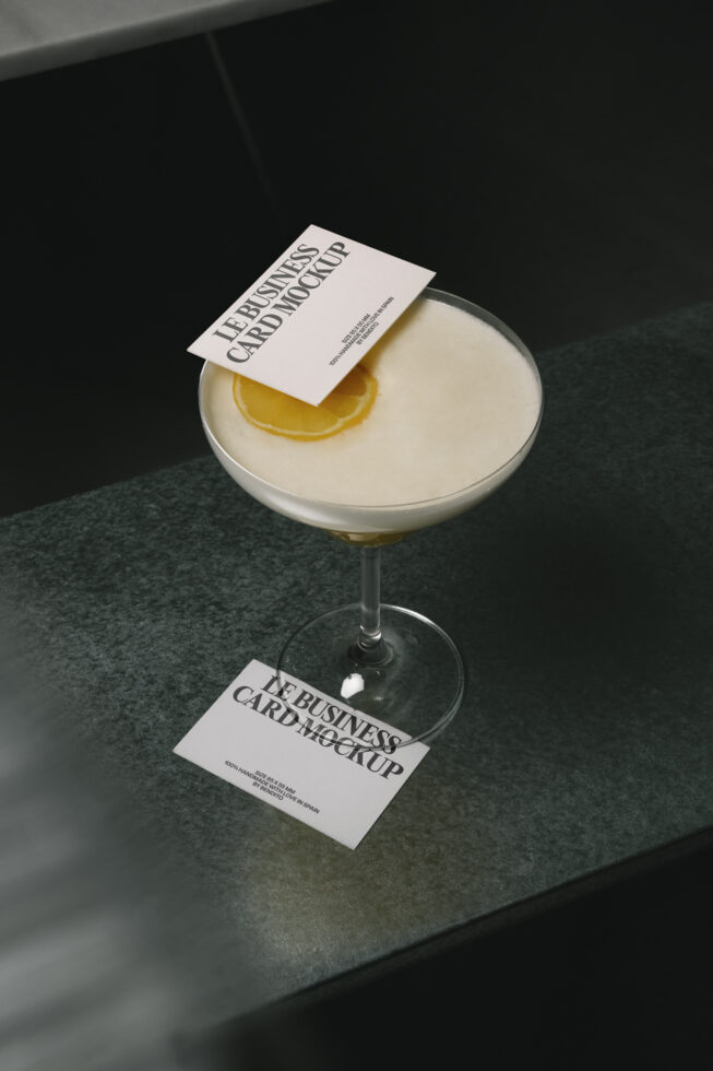 White business card mockup on cocktail glass with lemon slice, dark surface