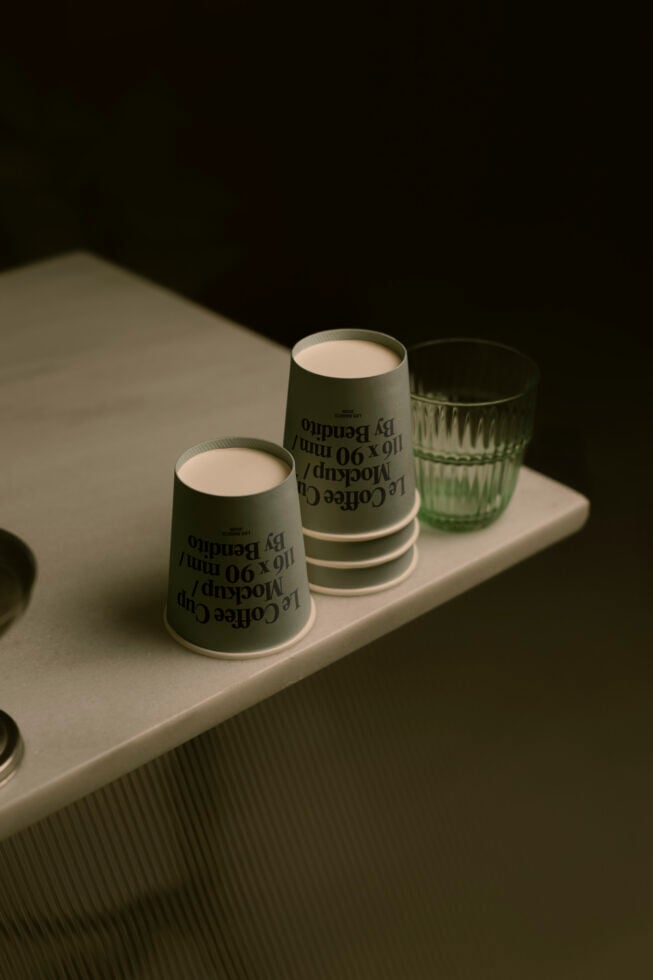 Two sage green paper cups with text print next to textured glass on white tray