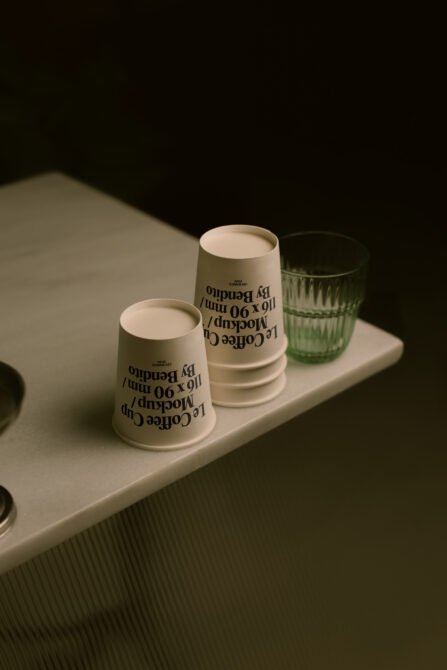 Sage green paper cups with typography print styled with green glass on white surface